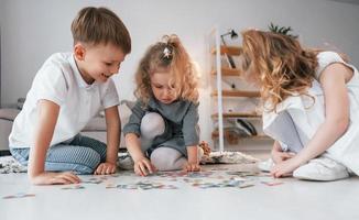 Sitting on the floor and playing game. Group of children is together at home at daytime photo