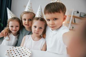 haciendo selfie celebrando el cumpleaños. grupo de niños está juntos en casa durante el día foto