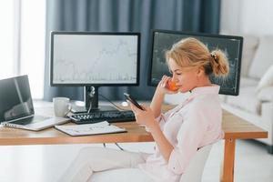 Reading information from smartphone. Female stock broker in formal wear is working in the office photo