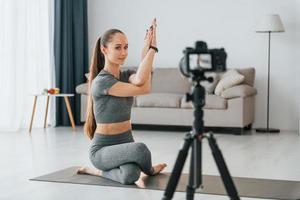 haciendo lecciones en cámara. mujer joven con cuerpo delgado y ropa de yoga está en casa foto