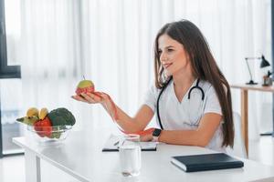 Conception of dieting. Holding apple. Professional medical worker in white coat is in the office photo