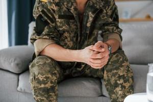 Close up view. Soldier in uniform is indoors in the domestic room photo