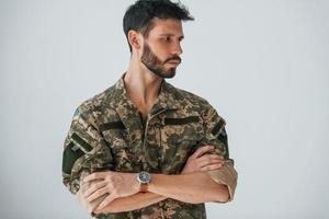 brazos cruzados. soldado en uniforme está de pie en el interior contra la pared blanca foto