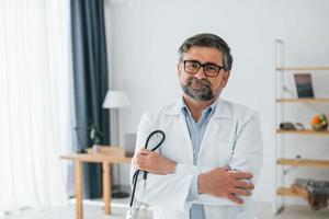 el médico varón está con estetoscopio. trabajador médico profesional con bata blanca está en la oficina foto