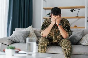 Having flashbacks. Post traumatic stress disorder. Soldier in uniform sitting indoors photo