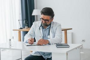 hombre escribiendo información en el documento. trabajador médico profesional con bata blanca está en la oficina foto