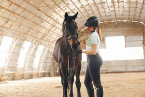 en sombrero protector. una joven vestida de jockey se prepara para un paseo con un caballo en un establo foto