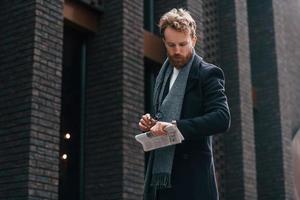 Holding newspaper in the hand. Stylish man with beard is outdoors near building photo