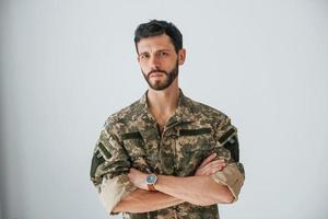 Soldier in uniform is standing indoors against white wall photo