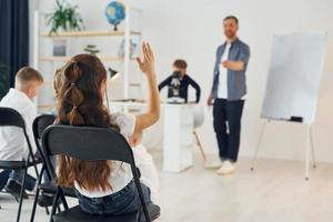 Boy with microscope, girl raises hand up. Group of children students in class at school with teacher photo