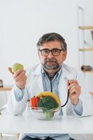 el médico varón está con una manzana. trabajador médico profesional con bata blanca está en la oficina foto