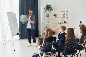 Teaching geography lesson by using Earth globe. Group of children students in class at school with teacher photo