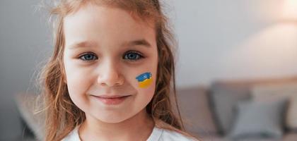 sonriendo y teniendo buen humor. retrato de niña con bandera ucraniana maquillada en la cara foto