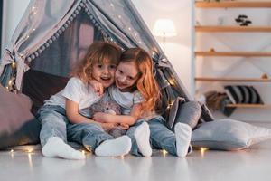 Embracing each other. Two little girls is in the tent in domestic room together photo