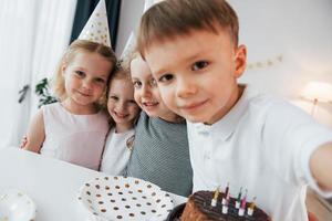 con pastel haciendo selfie celebrando el cumpleaños. grupo de niños está juntos en casa durante el día foto