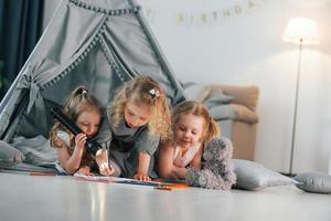 Laying down in the tent with flashlight and pencils to draw. Group of children is together at home at daytime photo