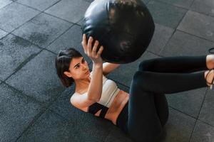 Black fitness ball. Woman in sportive clothes with slim body type is in the gym photo