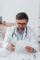 Man is busy with documents. Professional medical worker in white coat is in the office photo