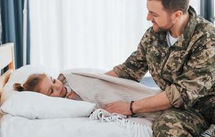 Peace and quiet. Soldier in uniform is at home with his little daughter photo