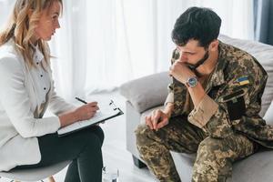 With notepad. Soldier have therapy session with psychologist indoors photo