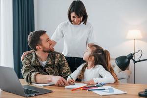 Sitting by the table. Soldier in uniform is at home with his wife and daughter photo