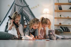 Girl holding flashlight. Other one draw on the ground with paper. Group of children is together at home at daytime photo