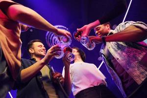 sosteniendo vasos en las manos. grupo de amigos divirtiéndose juntos en la discoteca foto