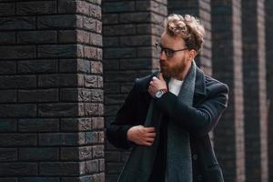 Stylish man with beard and in glasses is outdoors near building photo