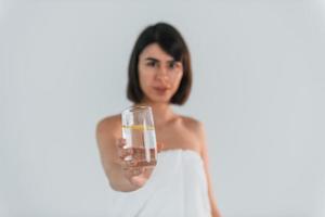 Holding glass with water. Young brunette is indoors against white background photo