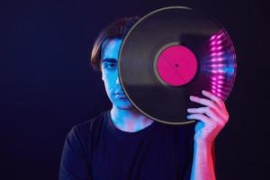 con disco de vinilo en las manos. hombre de pie en el estudio con luz de neón foto