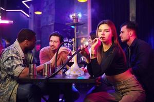 Hookah is on the table. Group of friends having fun in the night club together photo