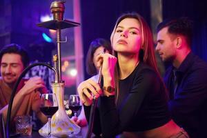 Hookah is on the table. Group of friends having fun in the night club together photo