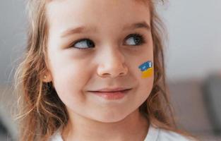 sonriendo y teniendo buen humor. retrato de niña con bandera ucraniana maquillada en la cara foto