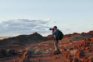 Using camera. Male tourist in casual clothes is in the deserts of Africa, Namibia photo