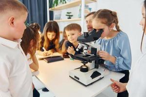 Girl looking into microscope. Group of children students in class at school with teacher photo