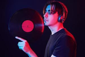 With vinyl record in hands. Man standing in the studio with neon light photo