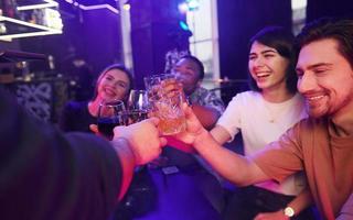 Sitting by the table together. Group of friends having fun in the night club photo