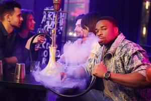 Sitting and smoking hookah. Group of friends having fun in the night club together photo