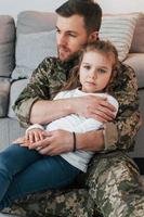 Finally meet each other. Soldier in uniform is at home with his little daughter photo