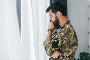 Ukrainian flag. Soldier in uniform is indoors in the domestic room photo