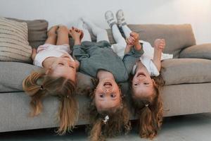 Girls laying down on the sofa upside down and smiling. Group of children is together at home at daytime photo