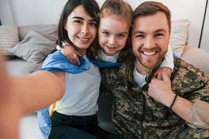 Making selfie. Soldier in uniform is at home with his wife and daughter photo