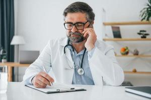 Man giving information by phone. Professional medical worker in white coat is in the office photo