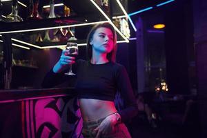 mujer joven de pie en el club nocturno con bebida en la mano foto