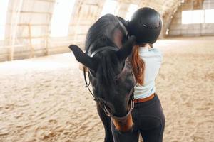 In protective hat. A young woman in jockey clothes is preparing for a ride with a horse on a stable photo