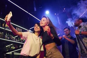 dos mujeres haciendo selfie. grupo de amigos divirtiéndose juntos en la discoteca foto