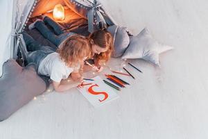 Writing S letter. Conception of learning and education. Two little girls is in the tent in domestic room together photo