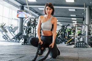 With special equipment. Woman in sportive clothes with slim body type is in the gym photo