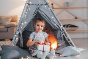 sosteniendo caja de regalo. linda niña jugando en la carpa que está en la habitación doméstica foto