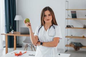 Woman holding an apple. Professional medical worker in white coat is in the office photo